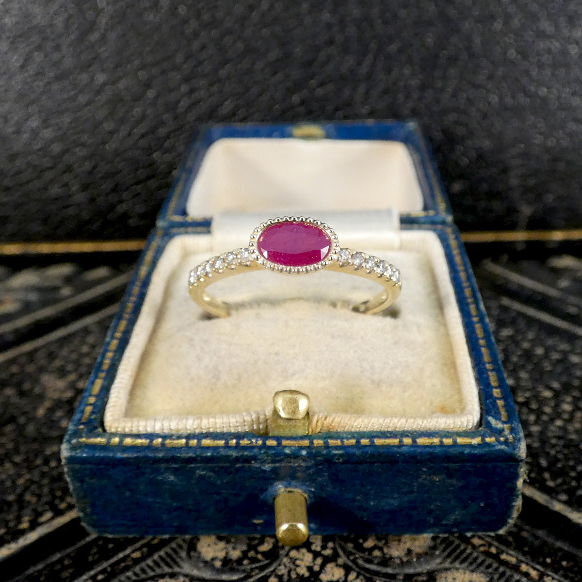Gold ring with a red gemstone in a blue velvet box on a textured surface