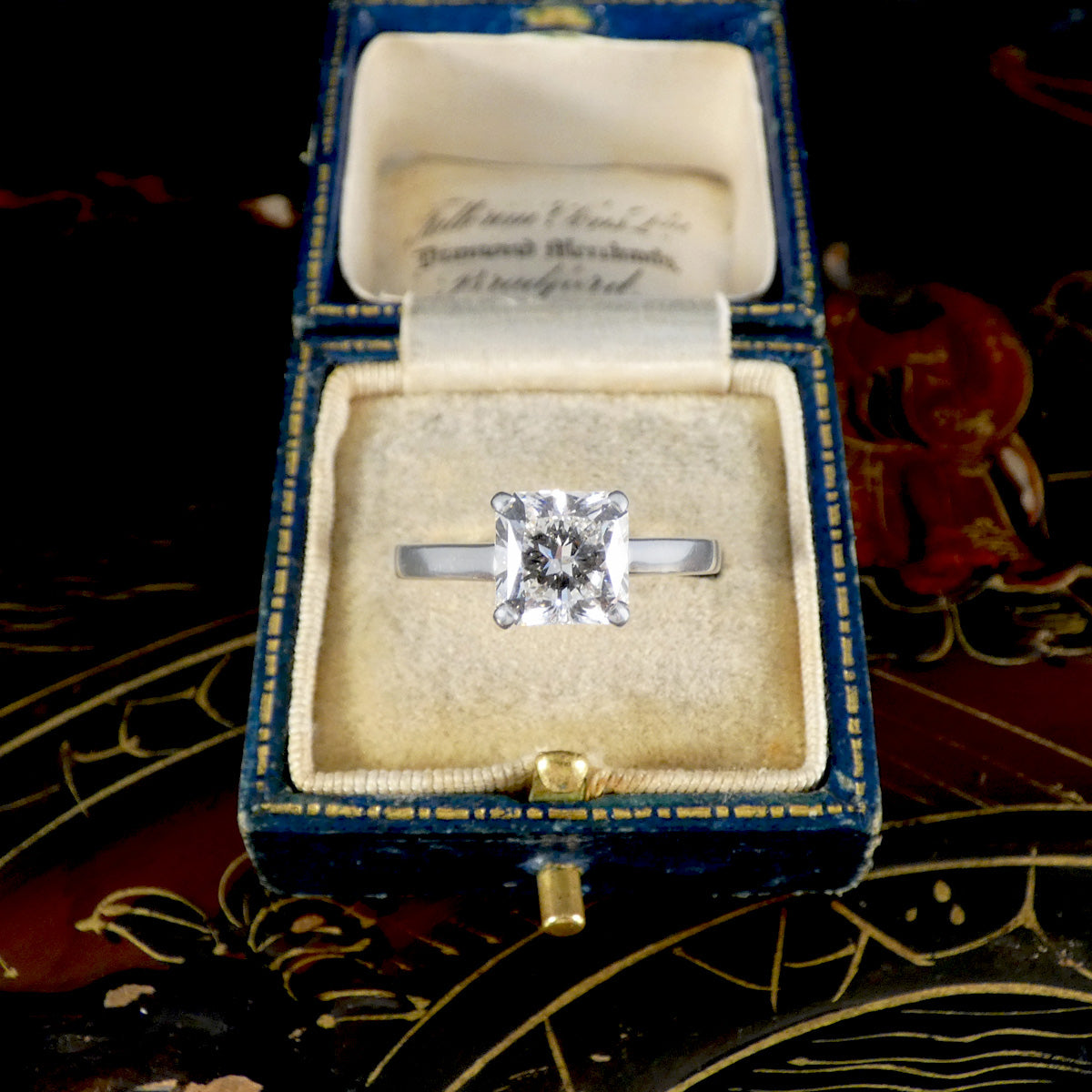 Diamond ring in a blue and gold box on a decorative surface