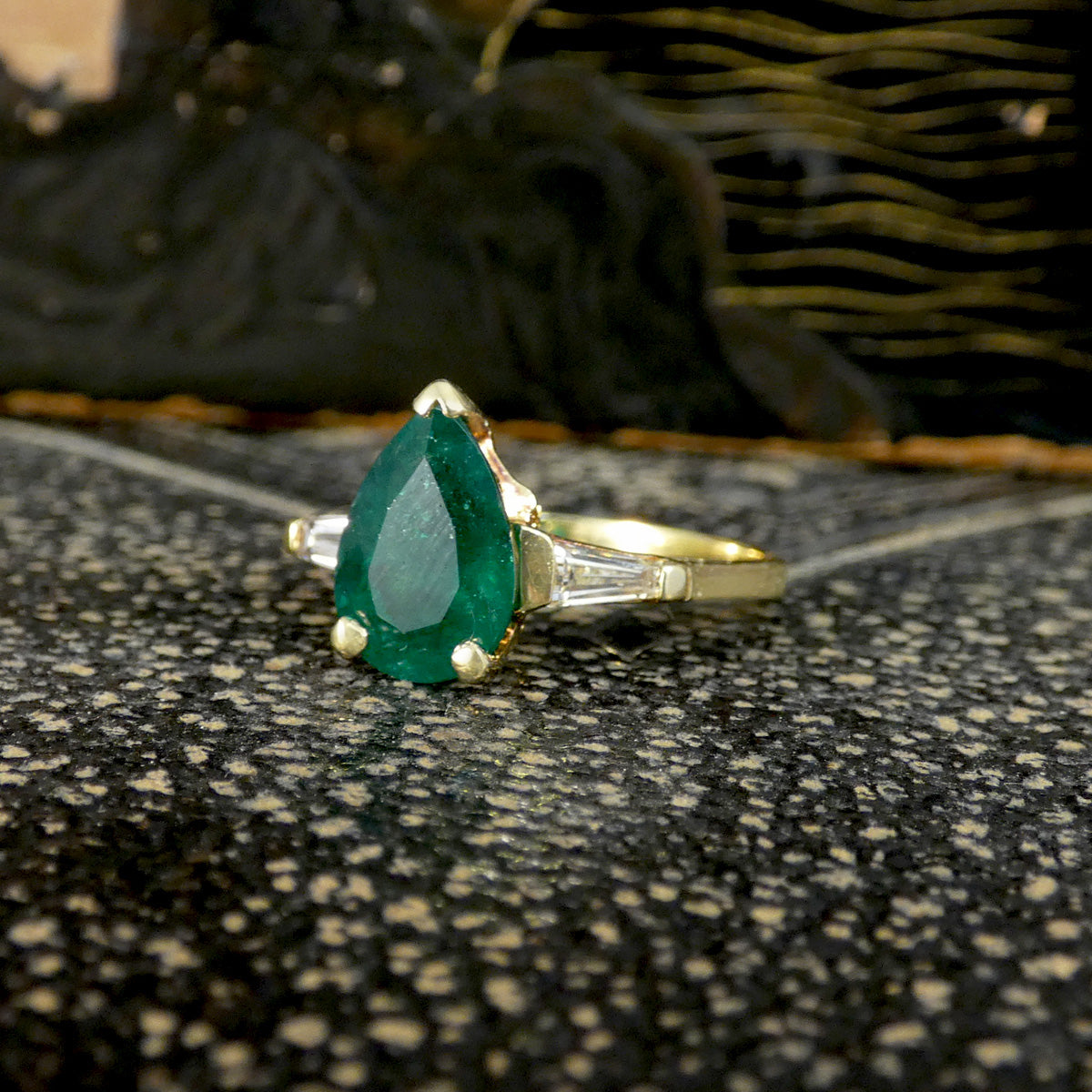 Gold ring with a green emerald and diamond gemstone on a textured surface