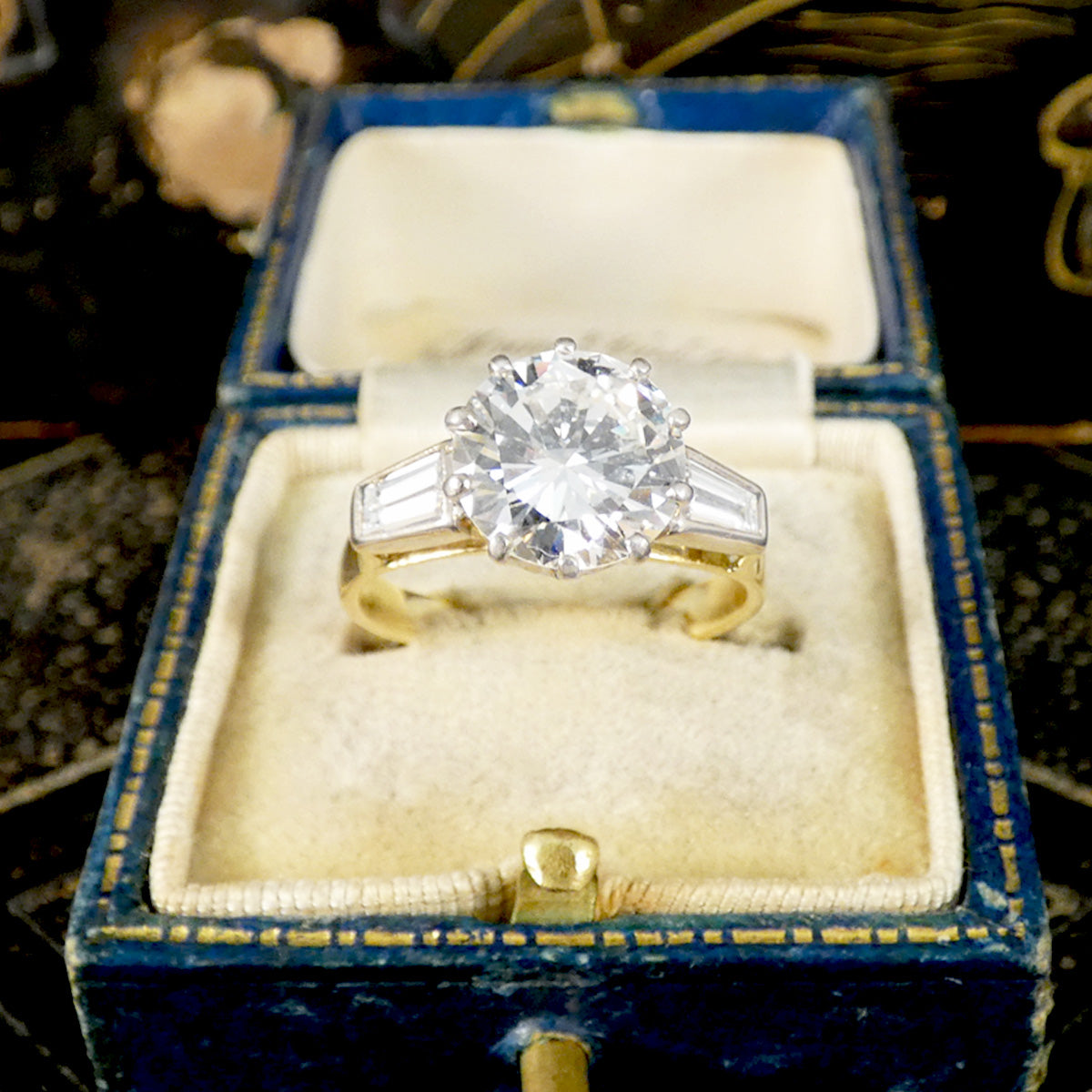 Large Diamond ring with tapered baguette cut shoulders in a blue velvet box on a dark background
