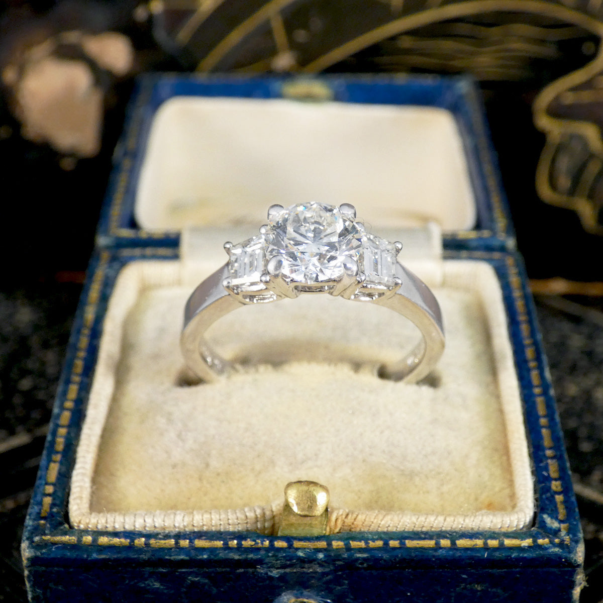 A brilliant cut and trapezoid cut Diamond three stone ring displayed in a vintage box.
