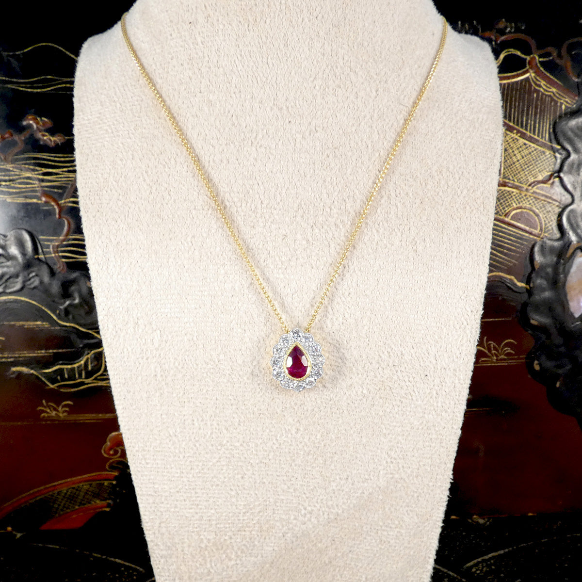 Gold necklace with a red ruby gemstone pendant on a mannequin bust.