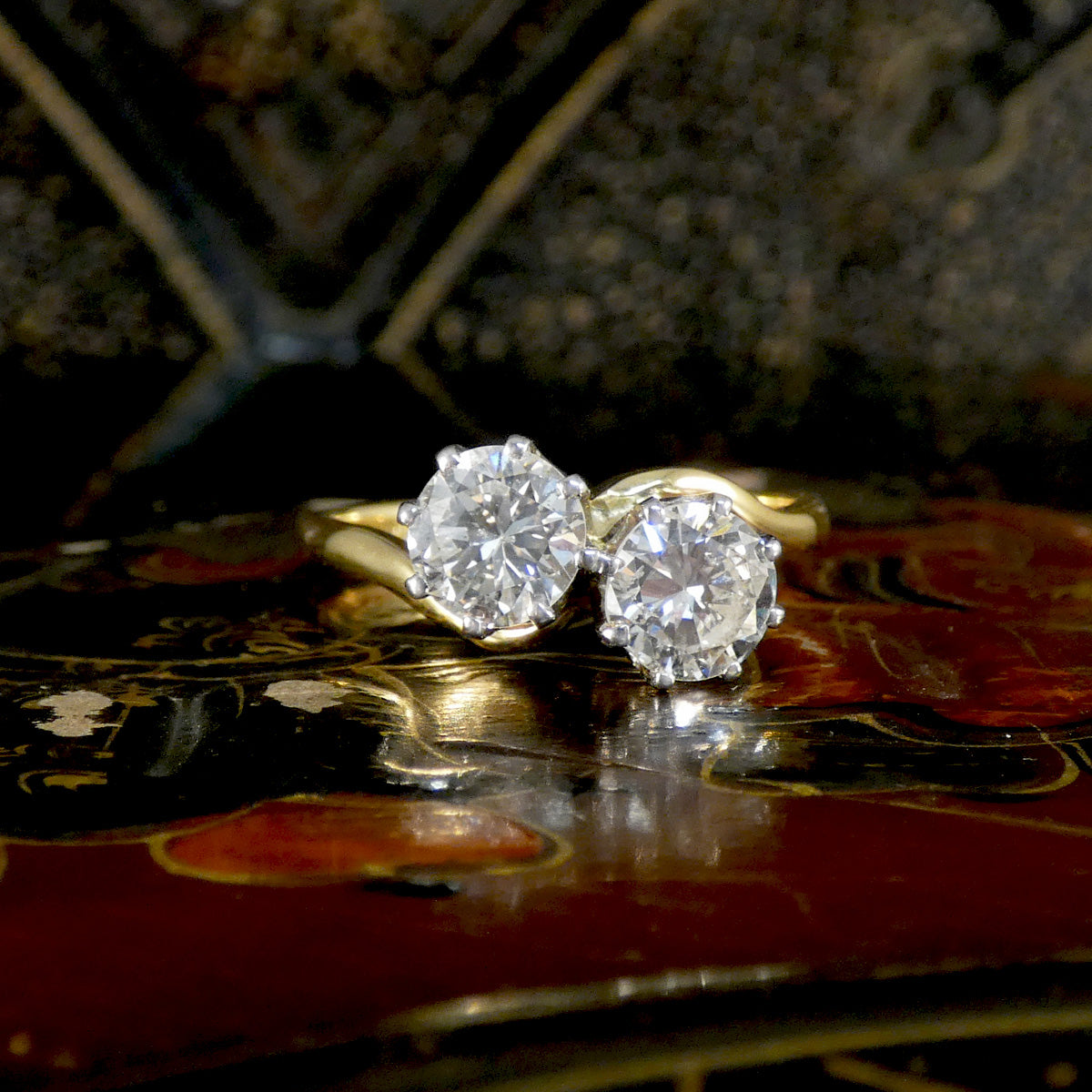 Gold ring with two large diamonds on a decorative surface