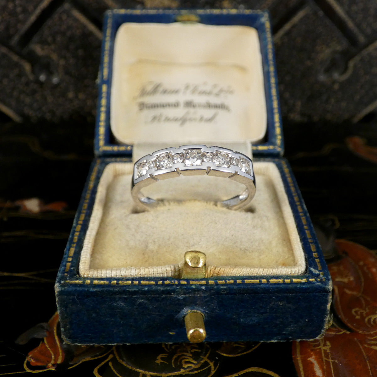 White Gold ring with diamonds in a chunky setting in a blue velvet box on a textured surface