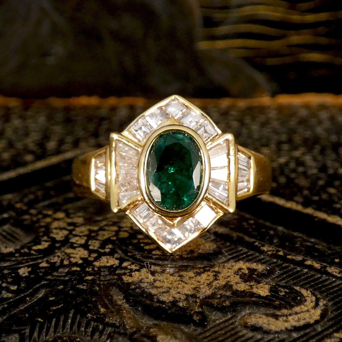 Elegant emerald and tapered diamond cluster ring set in yellow metal, testing as 18ct yellow gold, featuring a vivid oval emerald centre stone surrounded by shimmering tapered baguette diamonds.