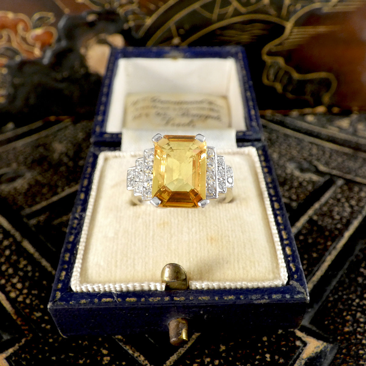 Ring with a yellow gemstone in a decorative box on a patterned fabric background