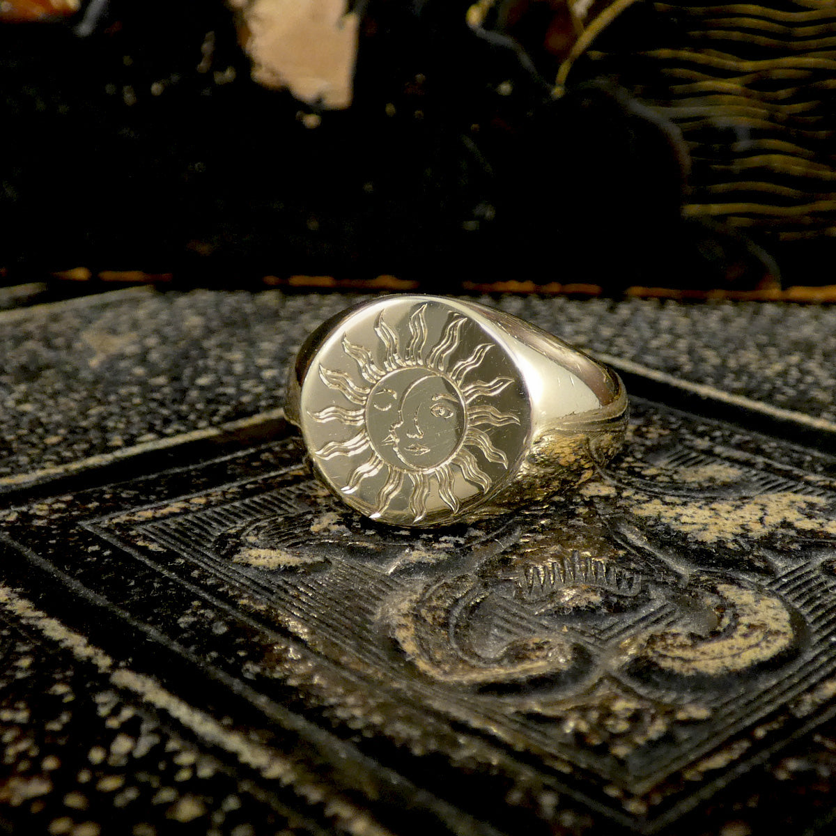 A solid yellow gold signet ring with a face engraved with a sun and moon on textured surface.