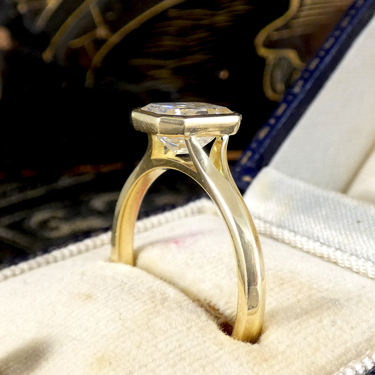 1.55ct Emerald Cut Diamond Solitaire in a Bezel Setting in 18ct Yellow Gold, showcasing a clear and bright diamond graded F/VS. Side view to showcase the open setting and wedfit design.
