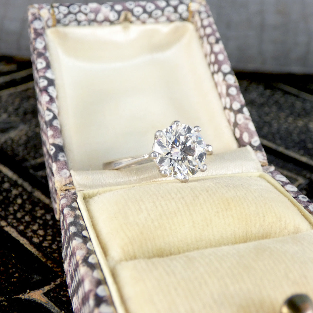 Diamond ring in an open jewelry box with a decorative lid.