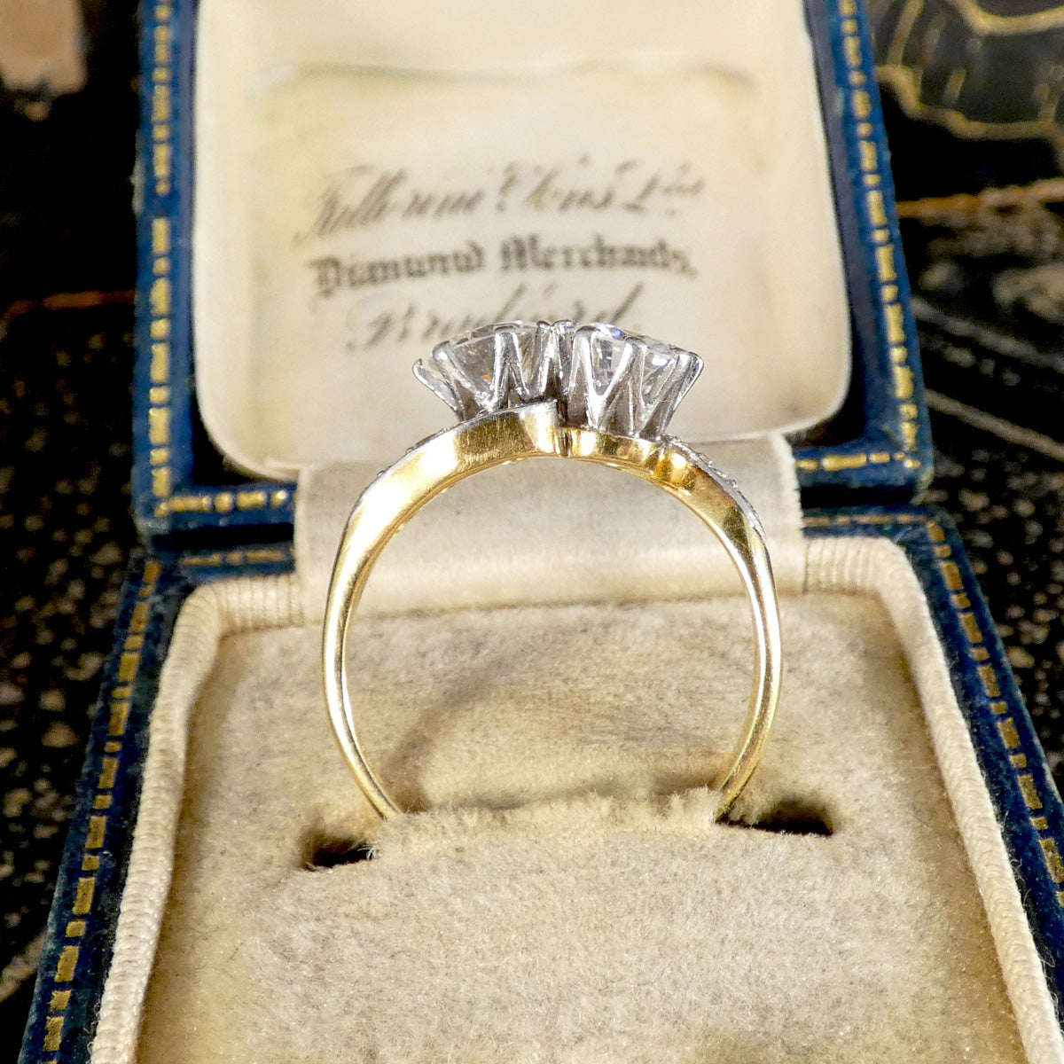 A vintage diamond ring with a yellow gold band and a silver-toned diamond setting, displayed inside an open antique blue velvet ring box.