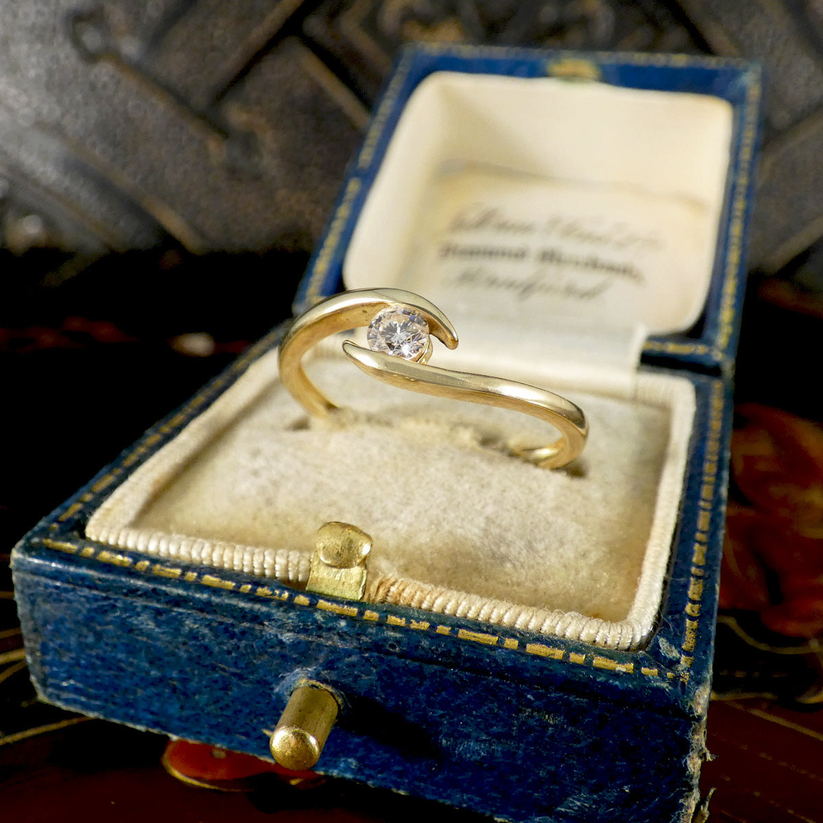 Gold ring with a diamond in an open blue jewelry box.