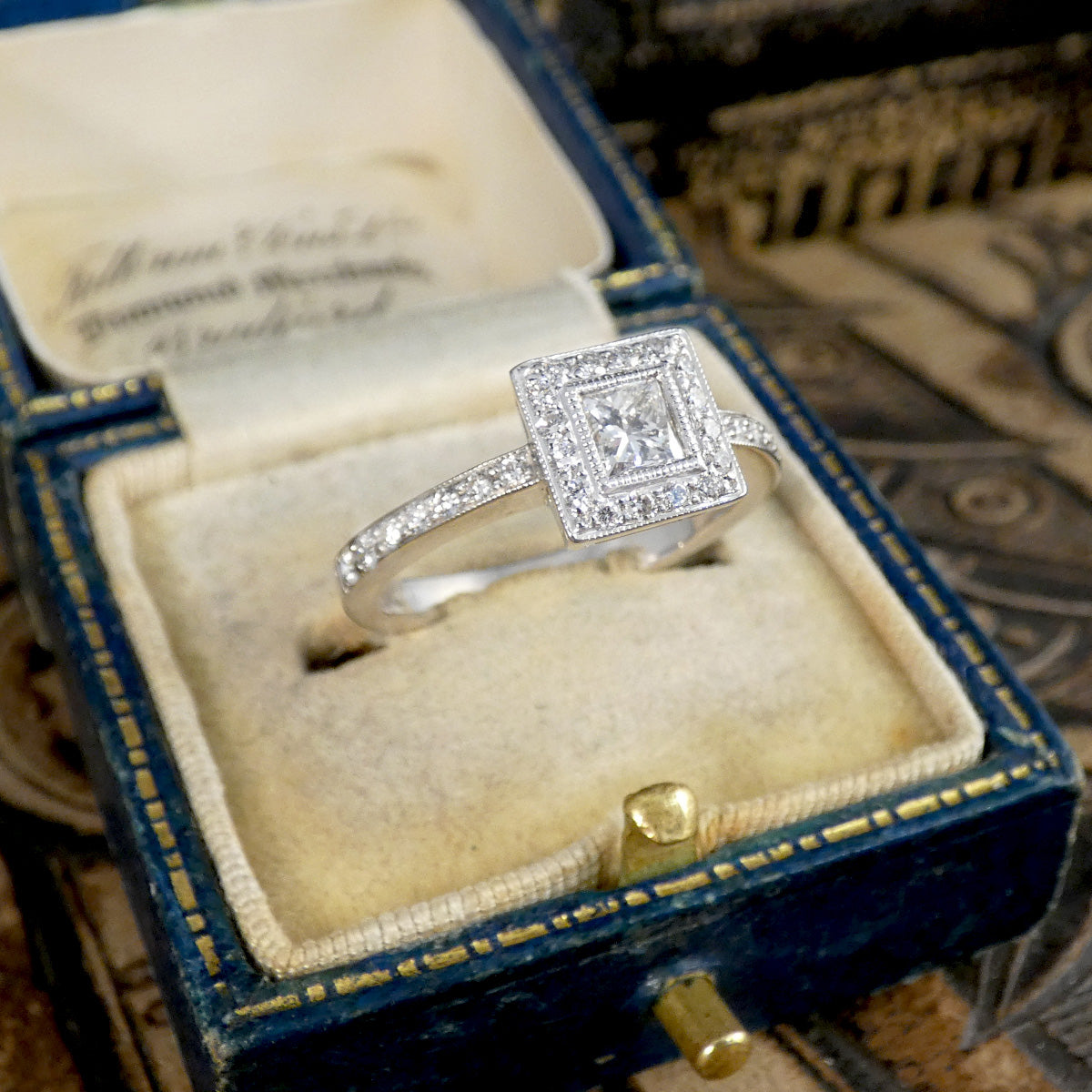 Diamond ring in a blue and gold jewelry box with an engraved lid.