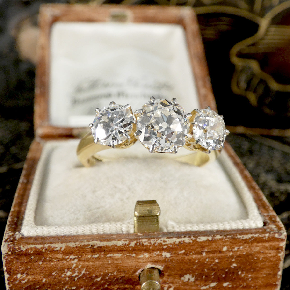 Three-stone diamond ring in a wooden box with a blurred background