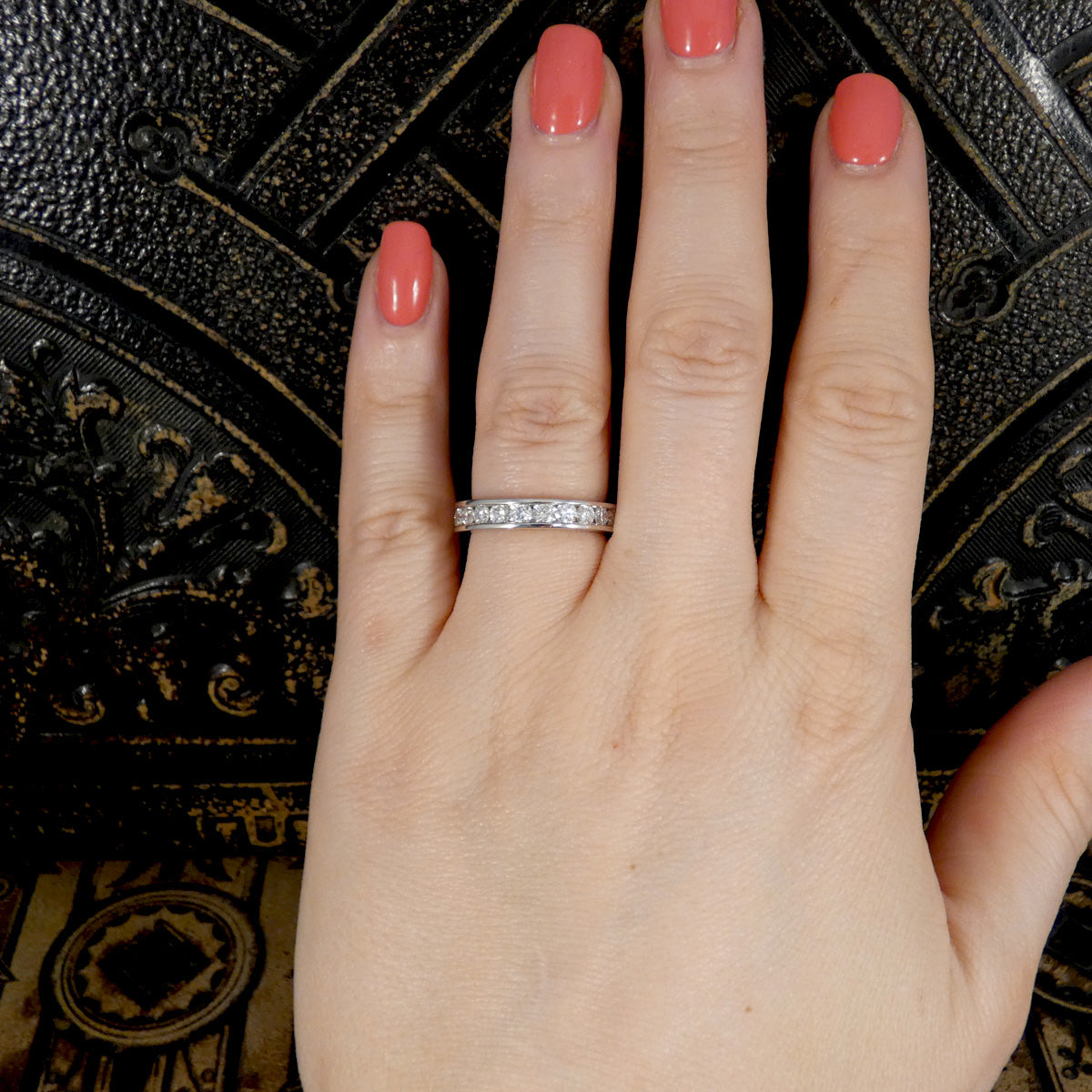 Hand wearing a diamond ring with pink nail polish against a dark textured background