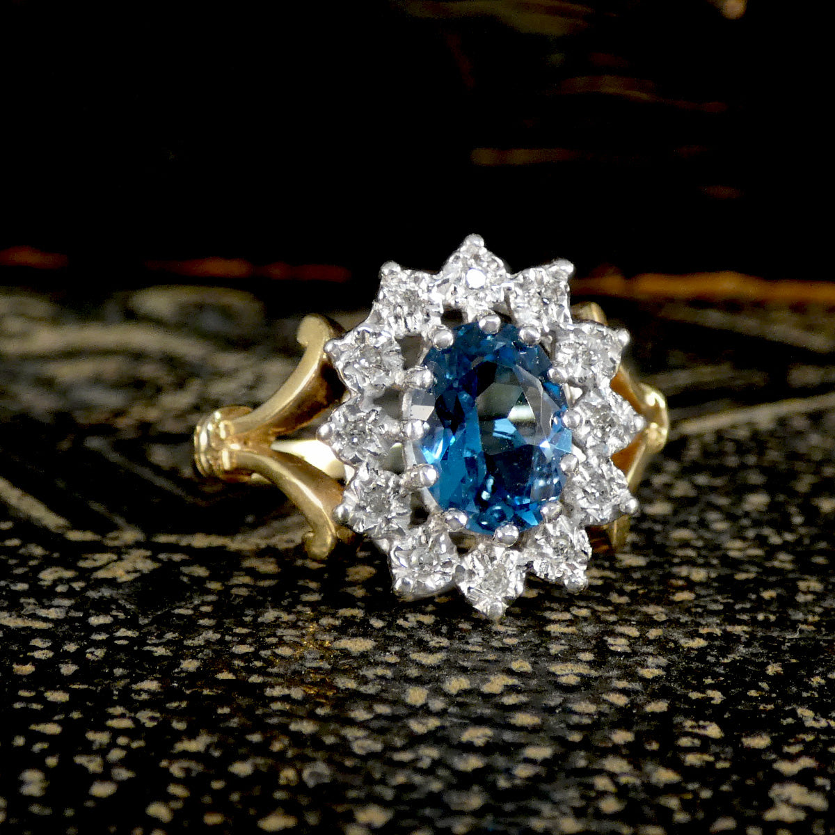 Gold and silver ring with a blue gemstone on a textured black surface