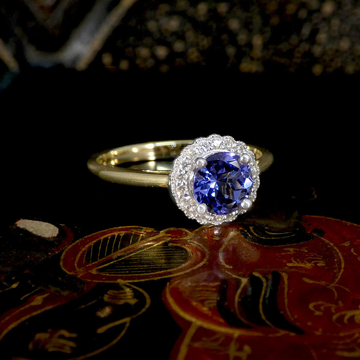 Ring with a blue gemstone and diamond halo on a reflective surface
