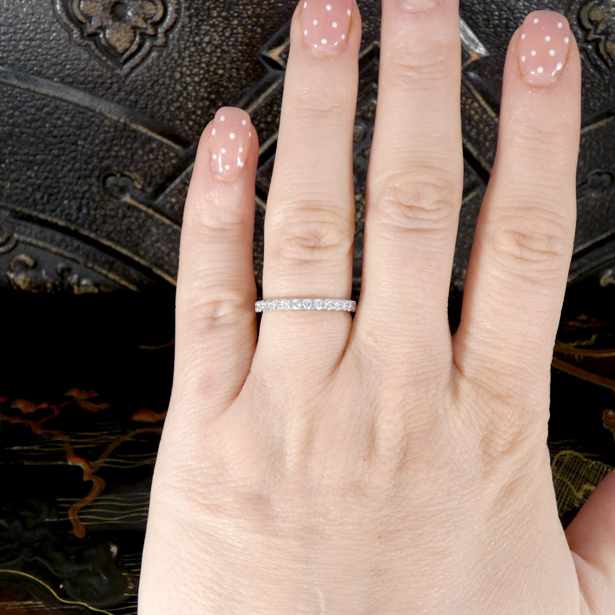 Hand wearing a diamond half eternity ring with a decorative background