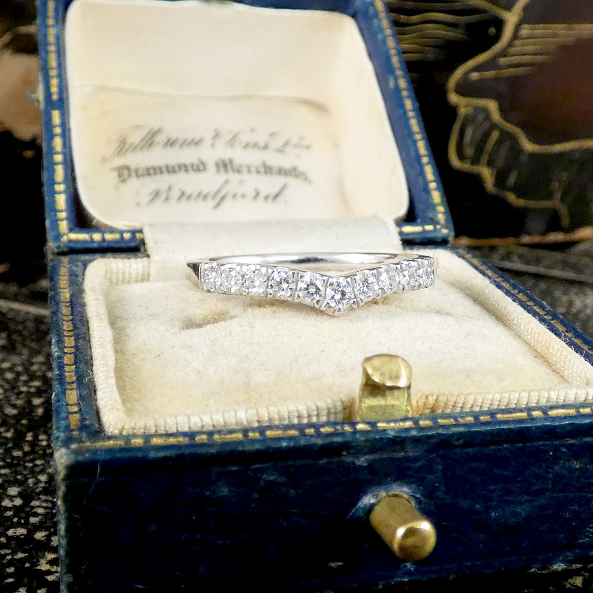 A vintage diamond ring set in a silver-colored band, displayed inside an open antique blue velvet ring box with a cream velvet insert. 