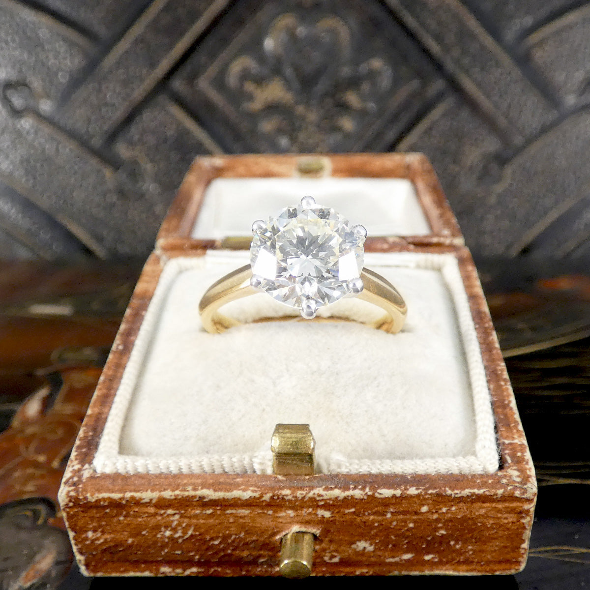 Gold ring with a large diamond in a wooden box against a textured background