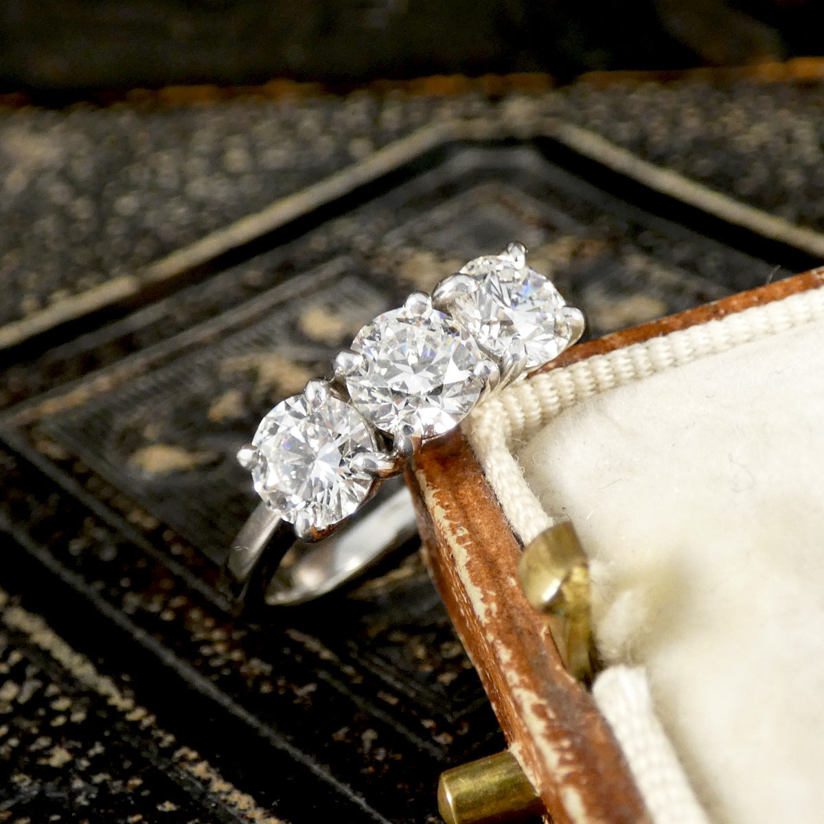 Three-stone diamond ring in a jewelry box with a textured background