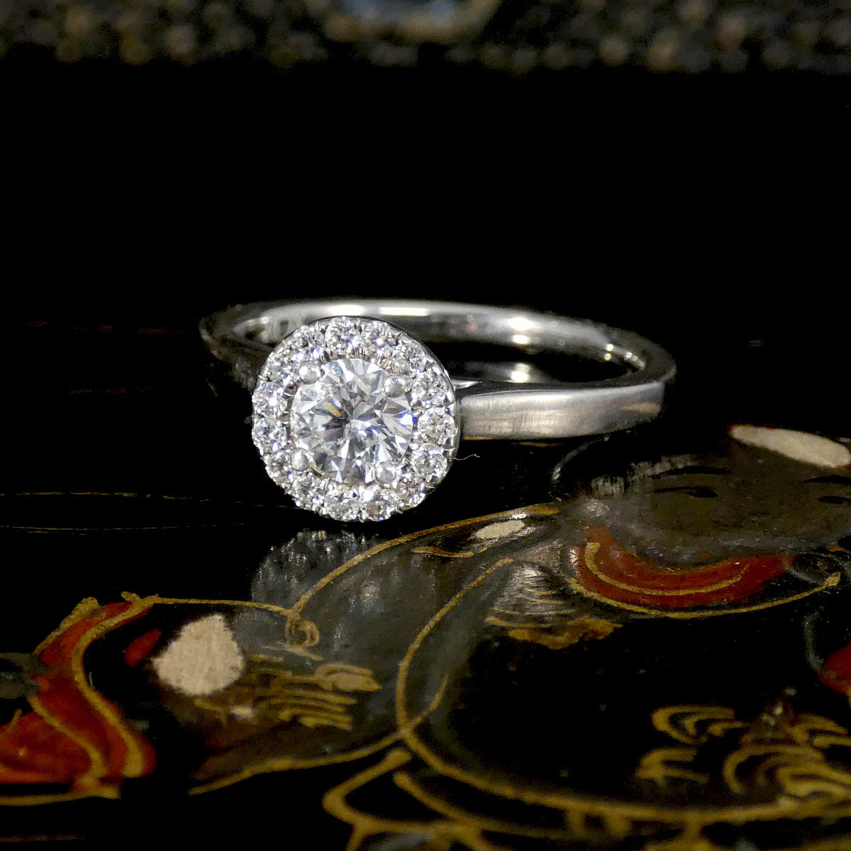 Silver ring with a large diamond on a reflective surface with a dark background