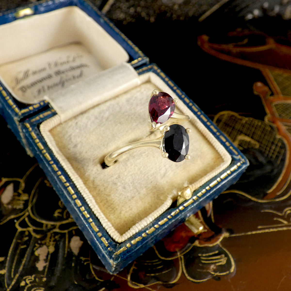 Gold ring with gemstones in a blue jewelry box on an ornate surface