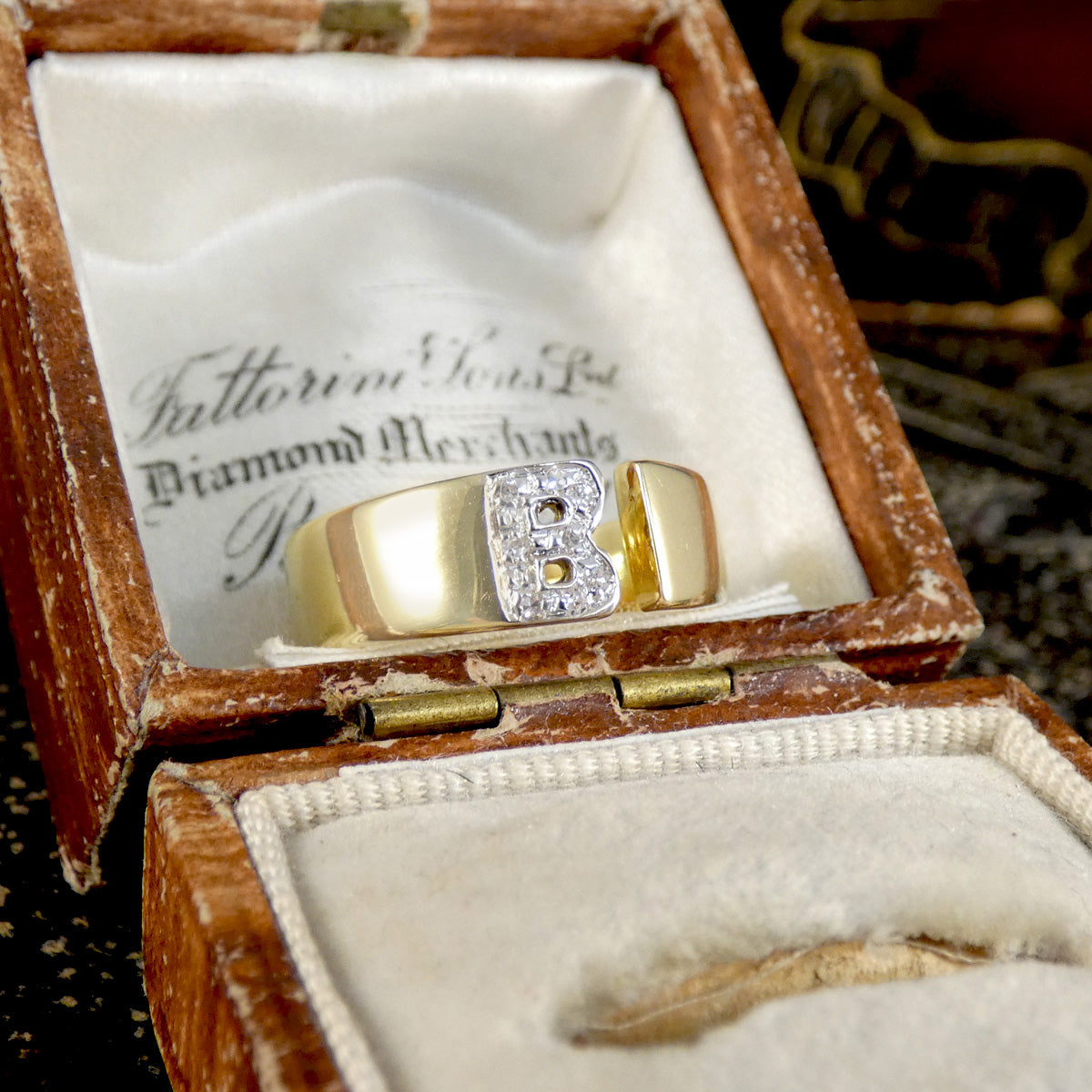 Gold ring with a letter 'B' in a wooden jewelry box