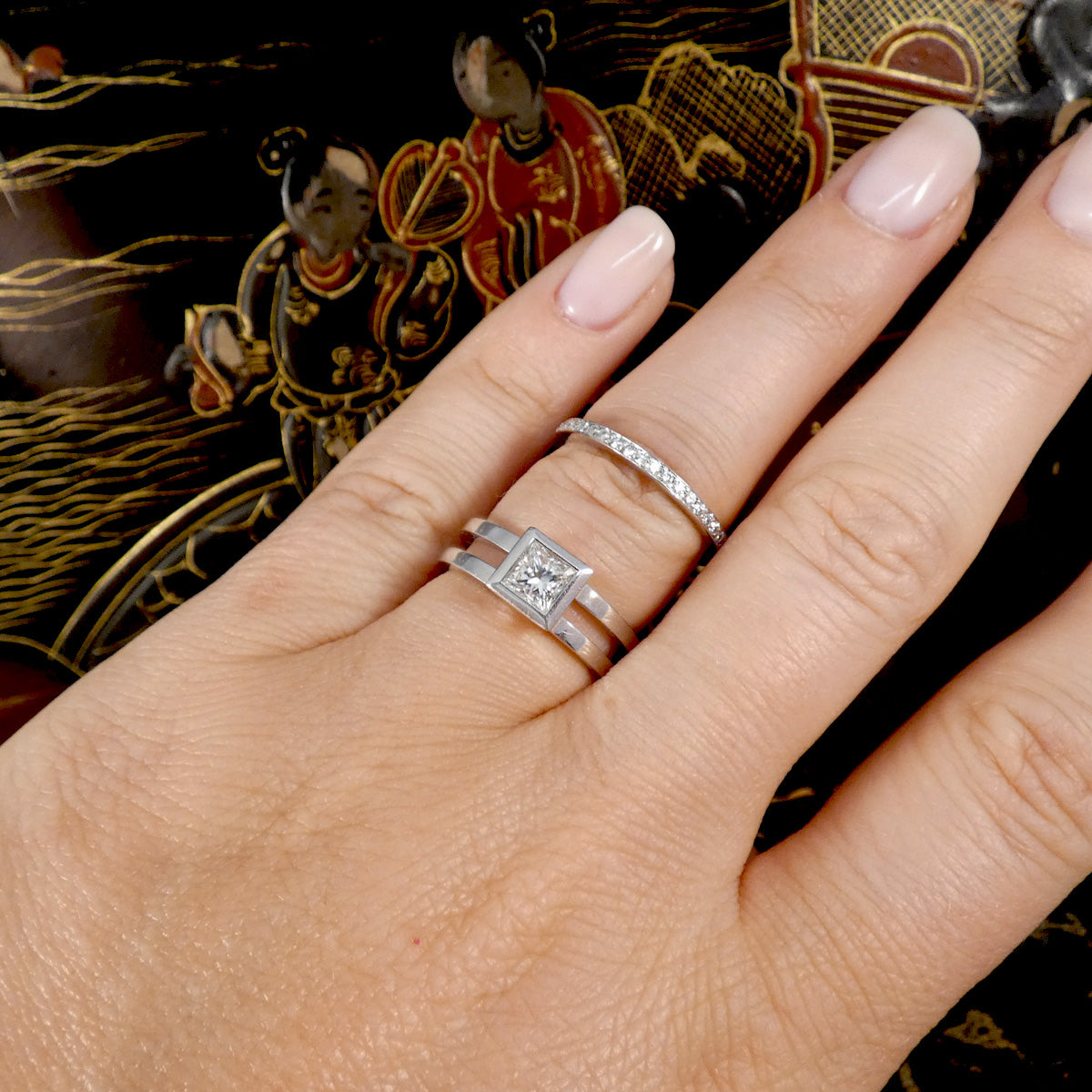 Hand wearing two diamond rings with a decorative background