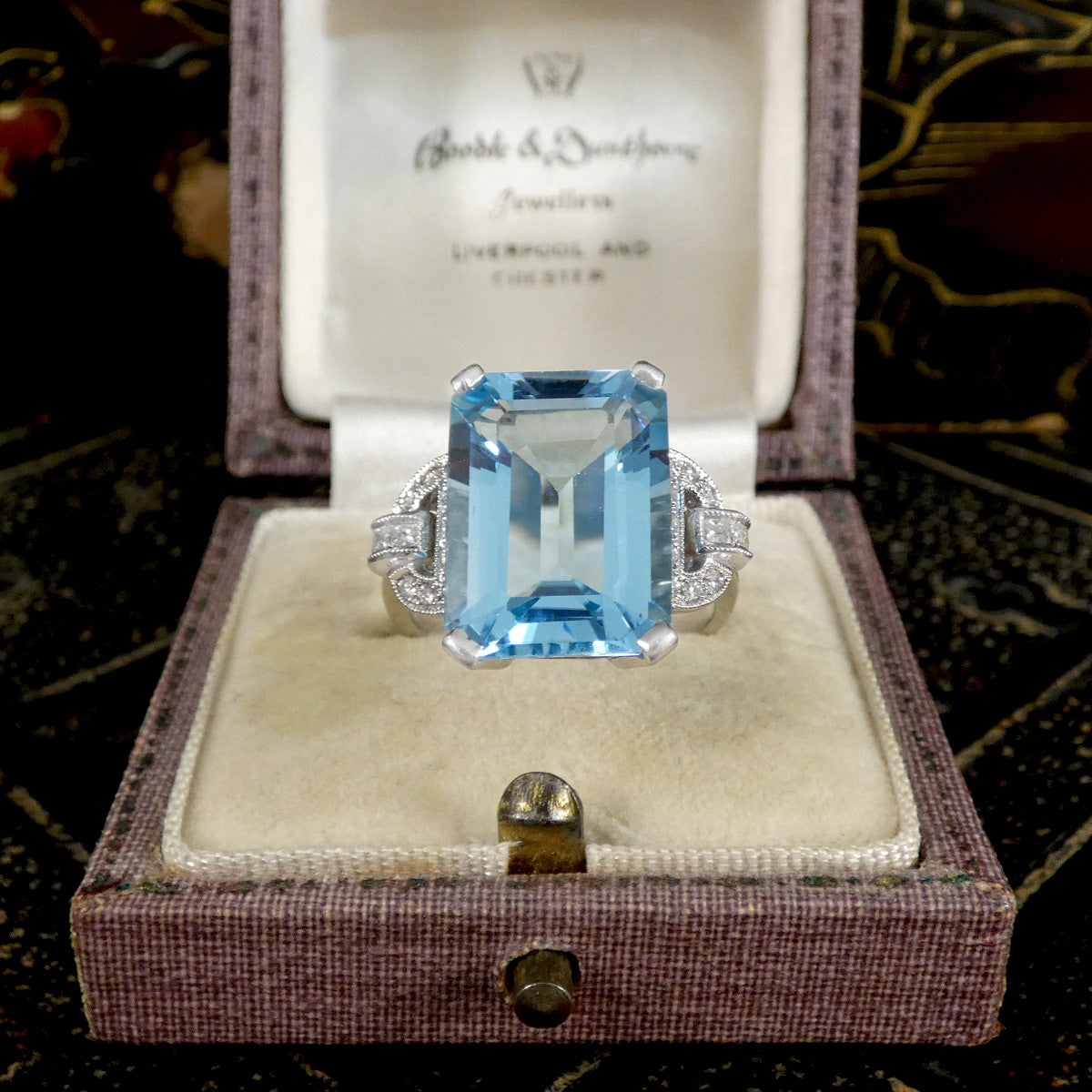 Ring with a blue gemstone in a jewelry box on a patterned background