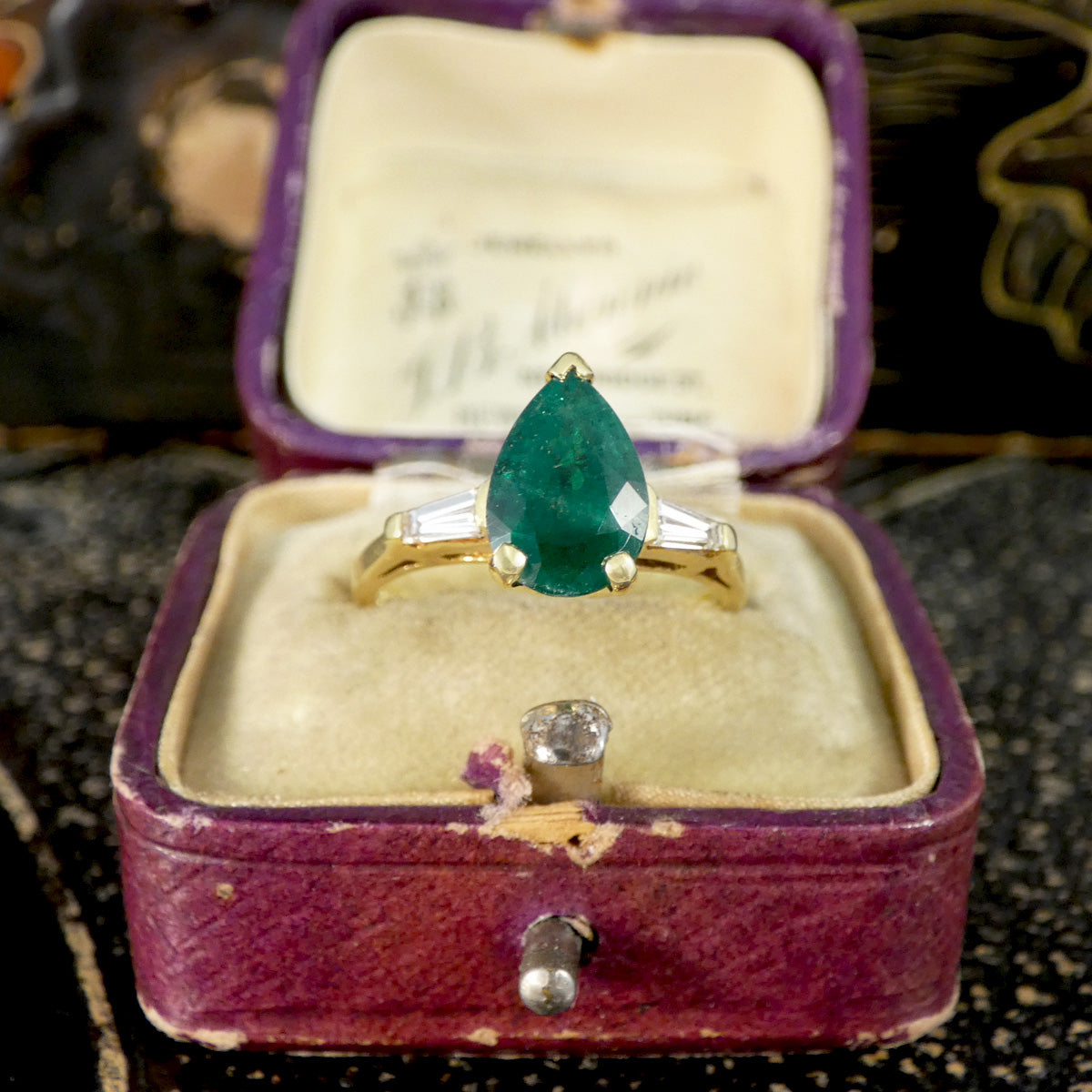 Gold ring with a green gemstone in an open purple jewelry box.