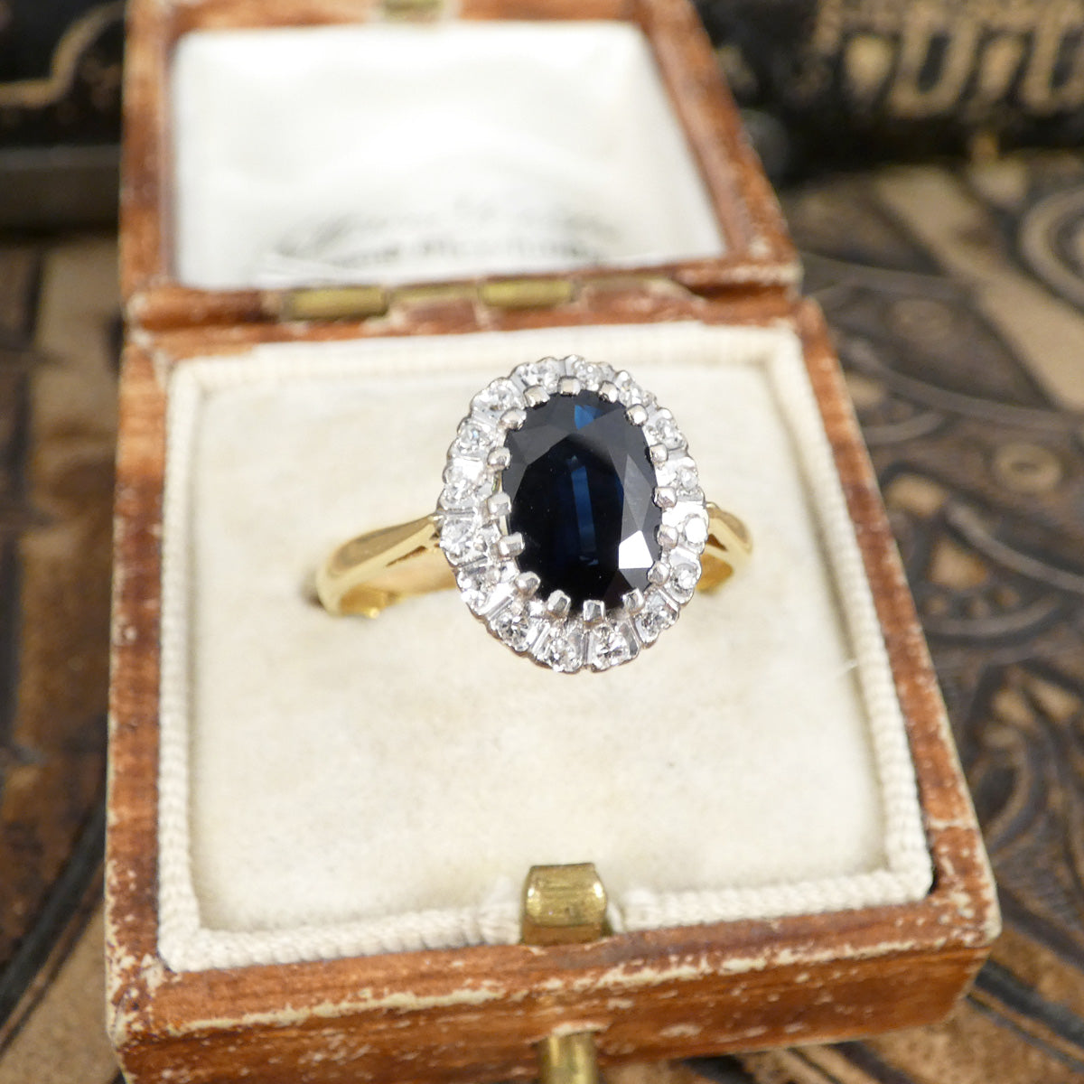 Gold ring with a blue gemstone and diamond accents in an open wooden box.