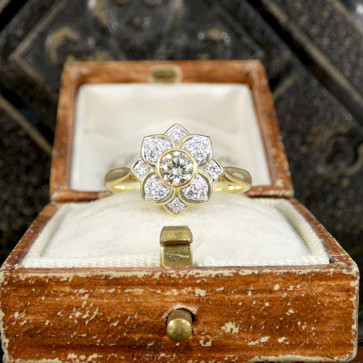 Gold ring with diamond flower design in an open wooden box.