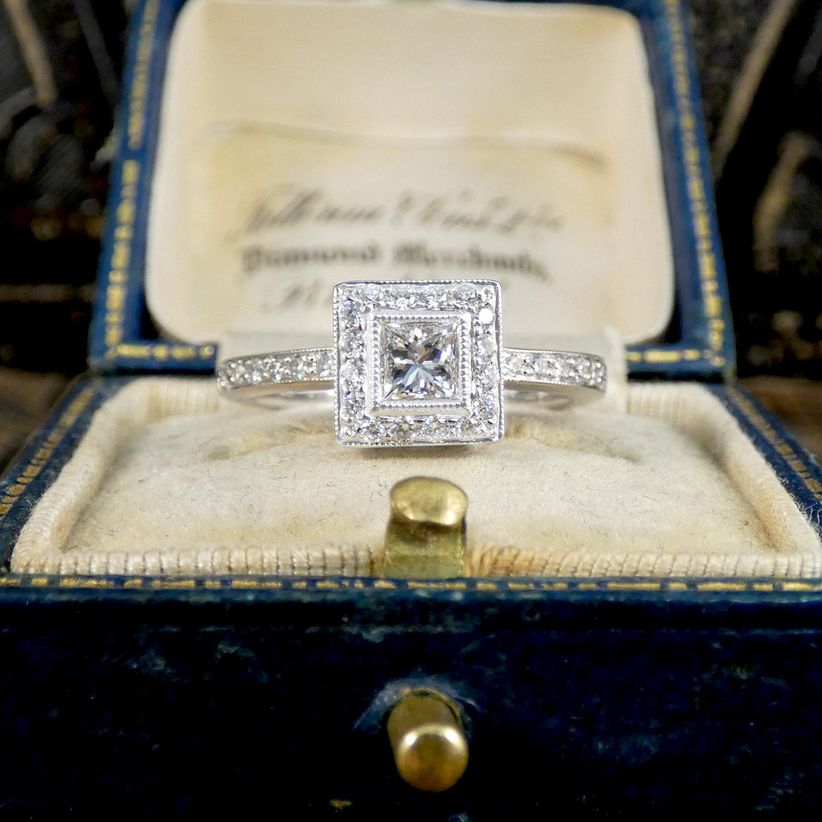 Diamond ring in a vintage jewelry box with an engraved lid.