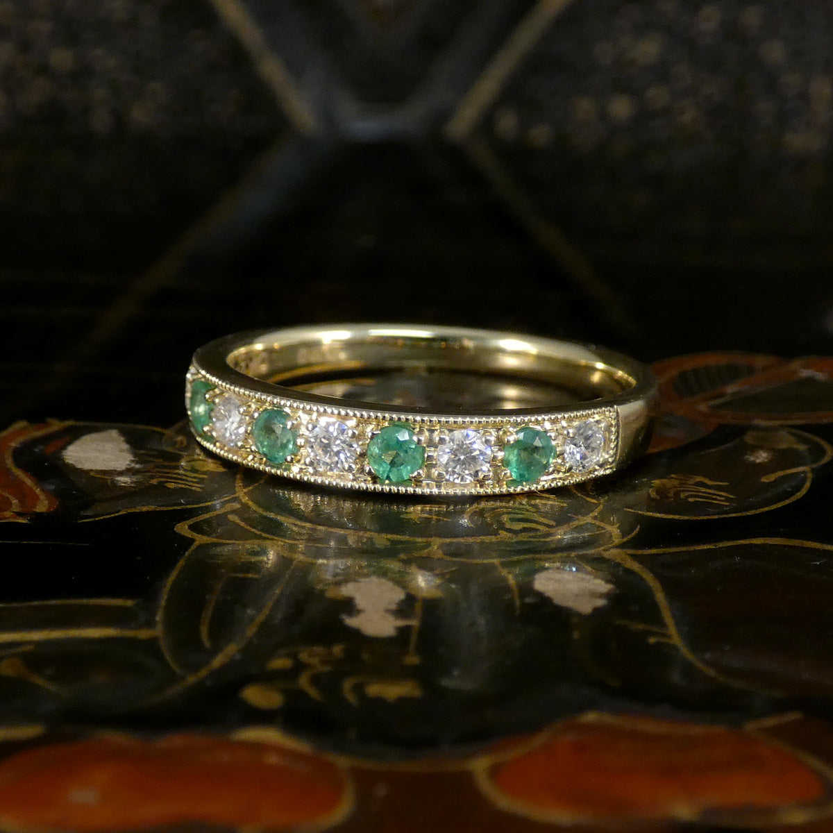 Gold ring with emeralds and diamonds on a reflective surface
