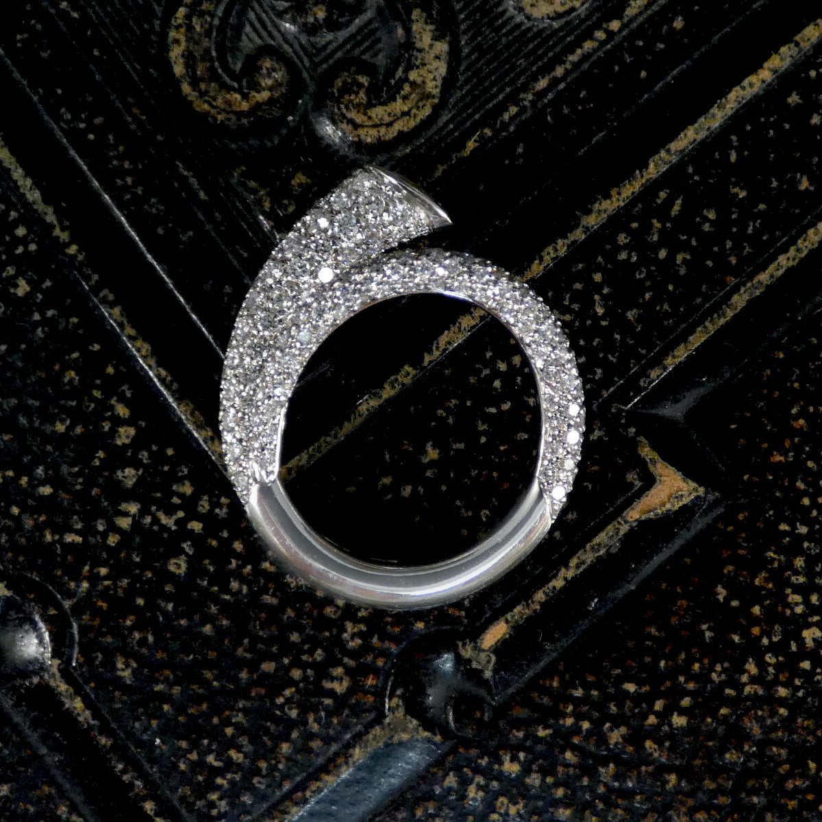 A unique diamond set snake like ring shown on a dark background.