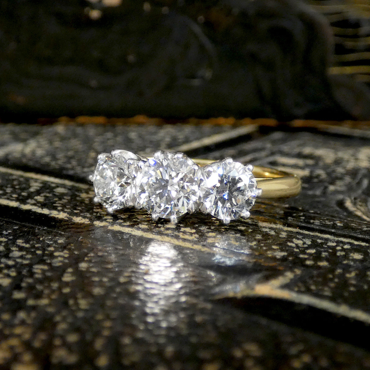 Gold ring with three diamonds on a textured surface