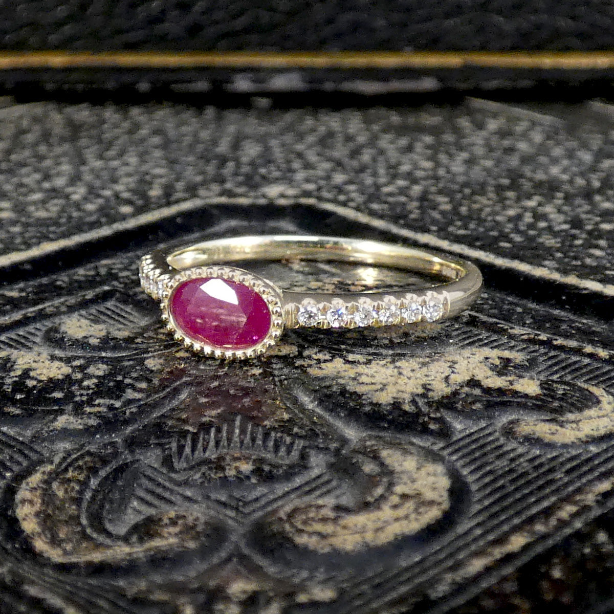 Gold ring with a red gemstone on an ornate black background