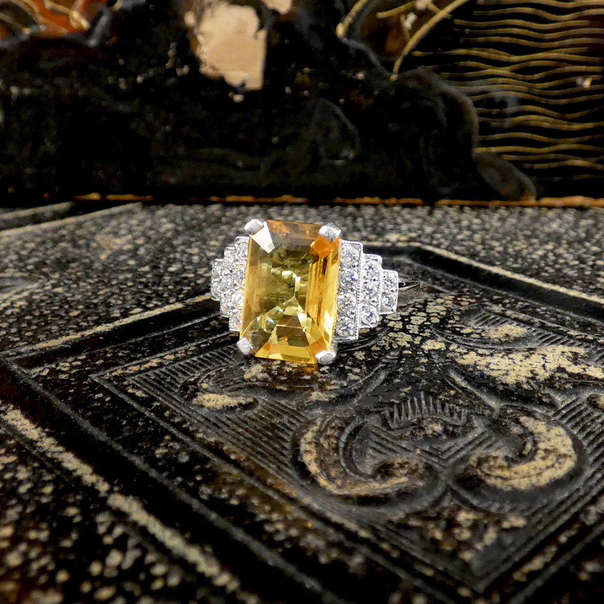 Ring with a yellow gemstone and diamond accents on an ornate black and gold surface