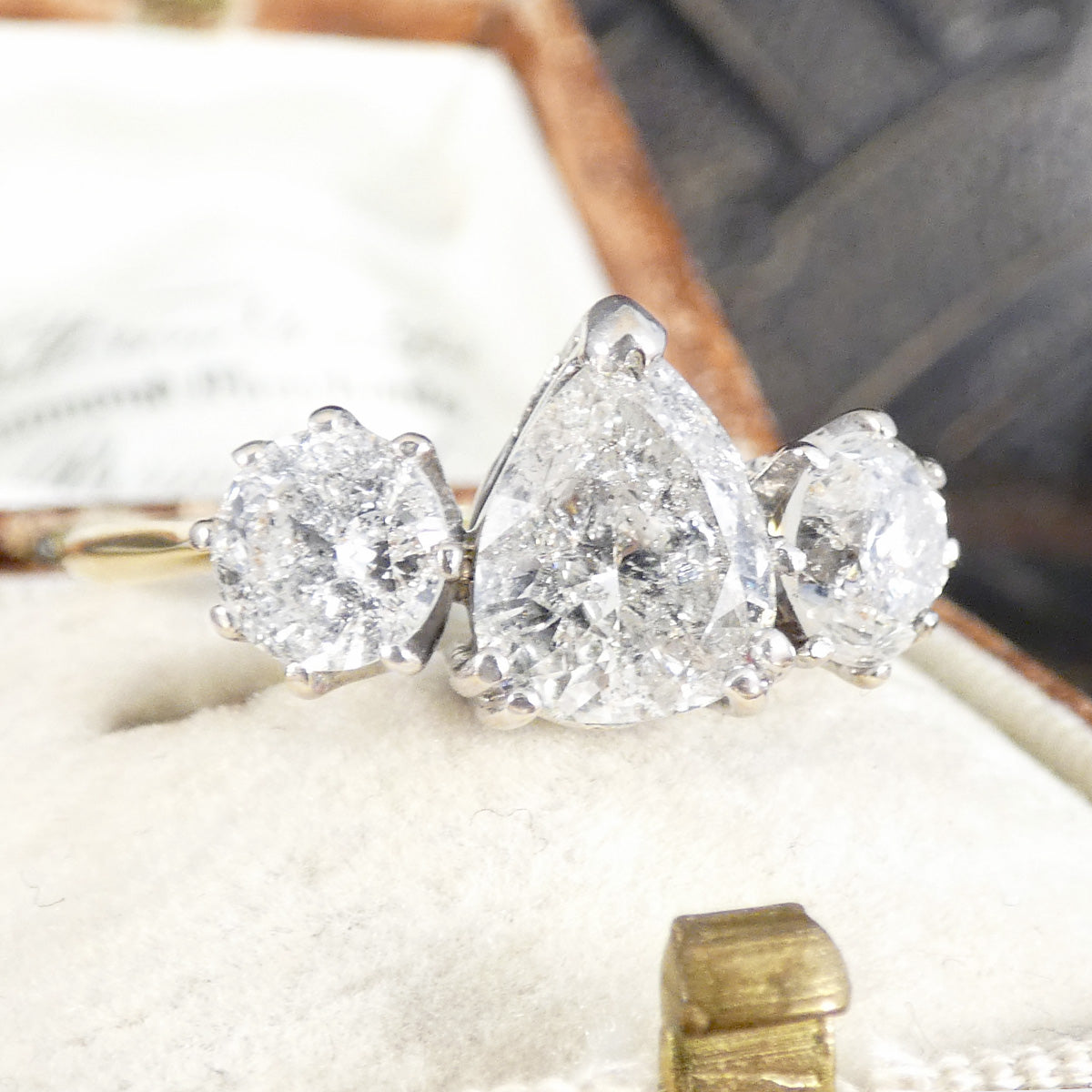 Close-up of a diamond ring with three included gemstones on a textured surface.