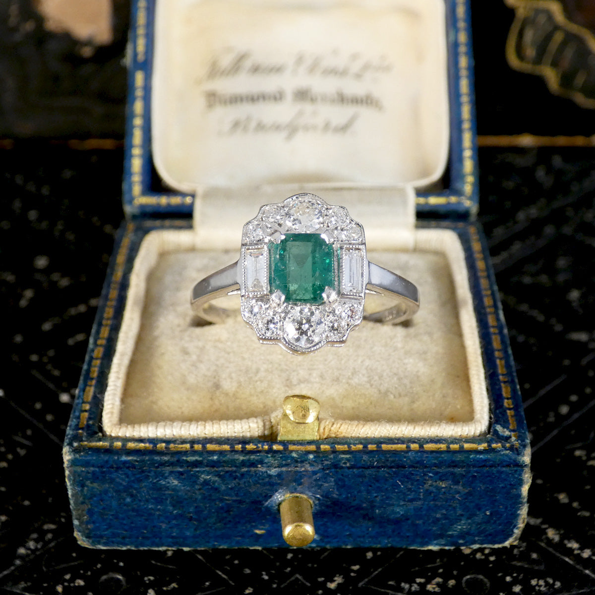 Art Deco Style Emerald and Diamond Cluster ring displayed in a vintage ring box.