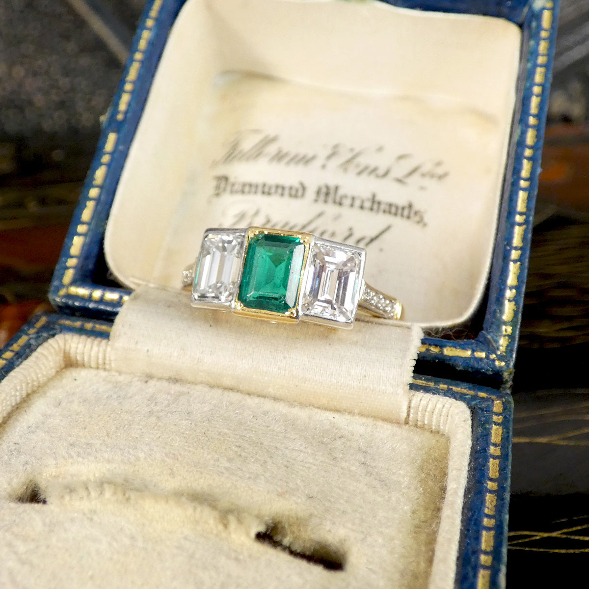 An Emerald and Diamond three stone ring in 18ct white and yellow gold displayed in a jewellery box.