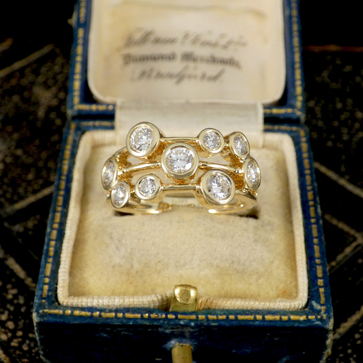 Gold bubble style ring with diamonds in an open jewelry box on a patterned background