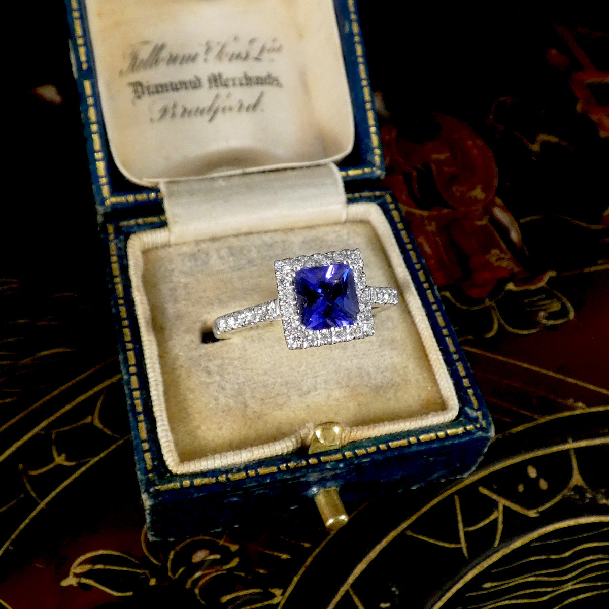 Diamond ring with a blue gemstone in an open jewelry box on a decorative surface.