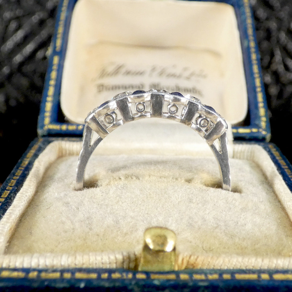 Underside view of platinum Art Deco-style diamond and sapphire ring, showcasing detailed openwork settings, displayed in a vintage blue velvet ring box.