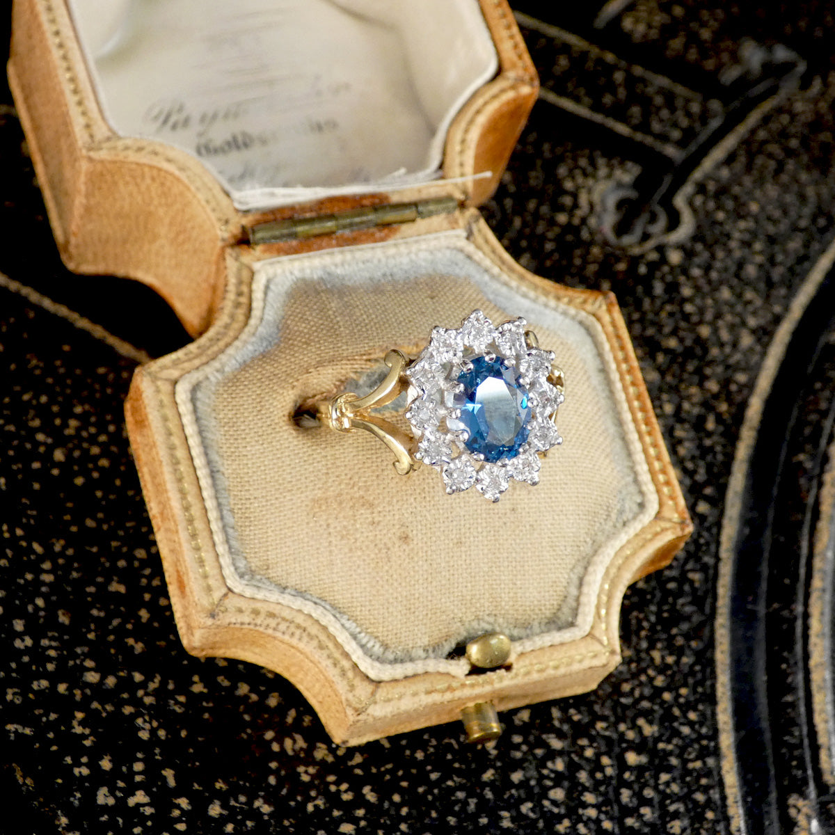Gold ring with a blue gemstone in an open jewelry box on a textured surface