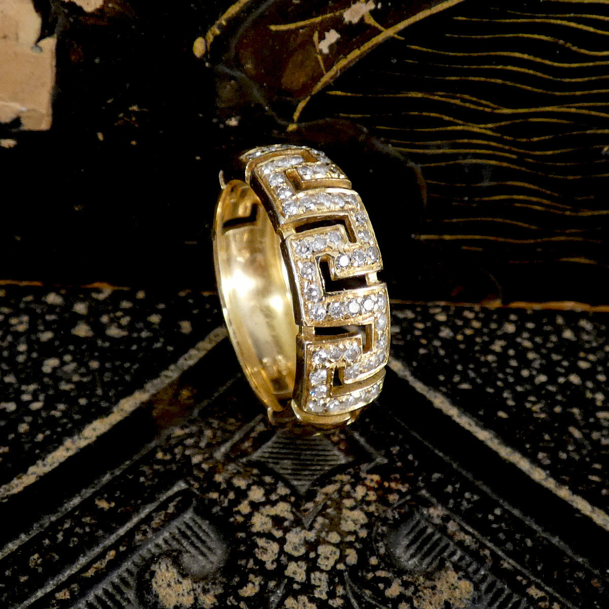Gold hoop earring with diamond accents on a textured black surface