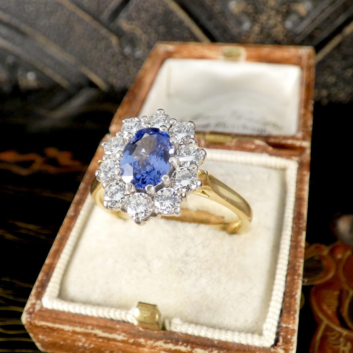 Gold ring with a blue gemstone and diamonds in an open wooden box.