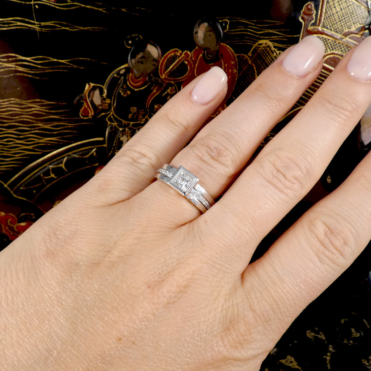 Hand wearing a platinum ring with a decorative background
