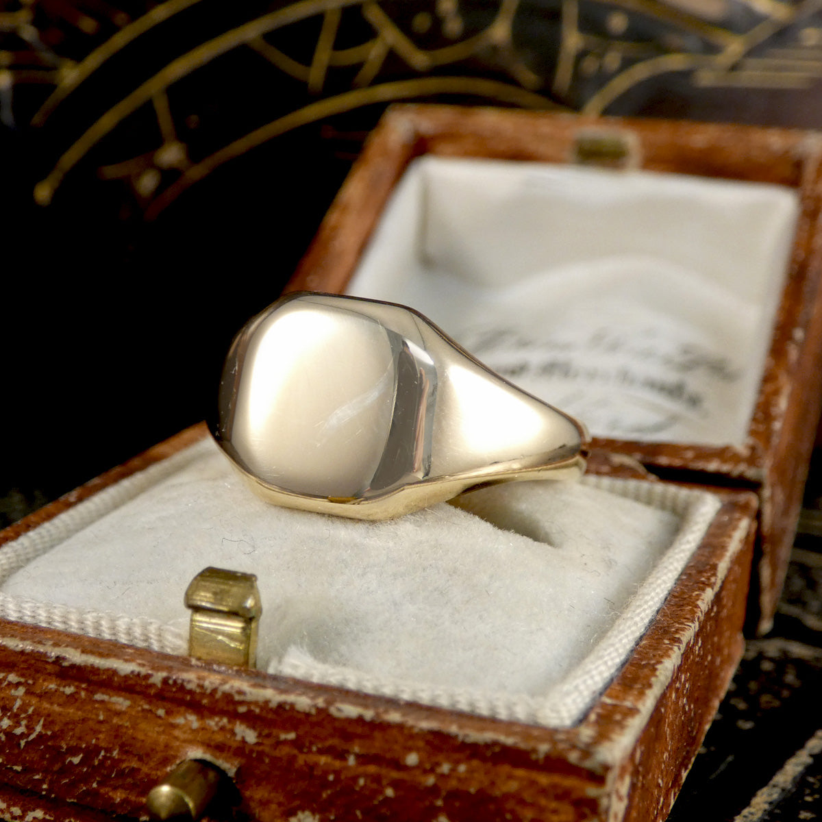 Gold signet ring in an open wooden jewelry box with a dark background