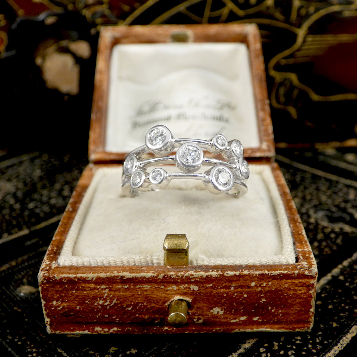 Platinum ring with diamonds in a wooden box on a textured surface